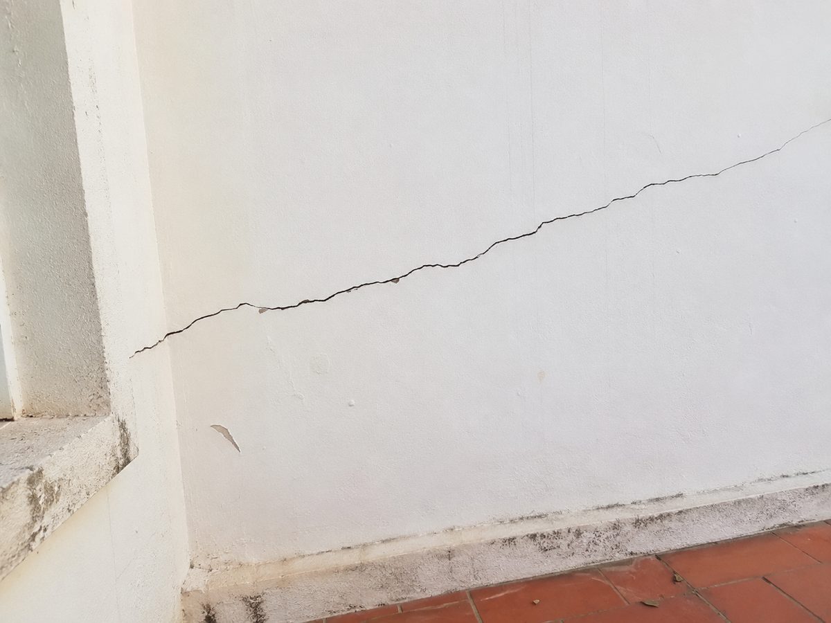 Rachadura na parede em linha contínua e levemente inclinada, partindo do canto superior de um vão, com bolor no rodapé